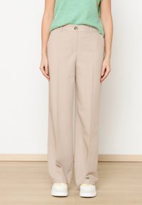 Bež široke hlače z gladko teksturo, z zapiranjem na gumb spredaj in poševnimi stranskimi žepi, v kombinaciji z belimi supergami.