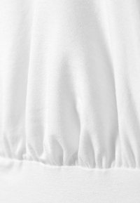 White cotton fabric showcasing a gathered texture at the bottom seam, with a smooth, lightweight feel throughout.