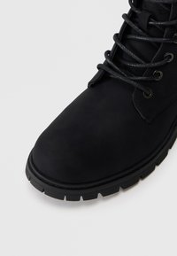 Bottines noires avec une texture lisse, bout rond, œillets métalliques et lacets noirs. Semelle en caoutchouc crantée pour une bonne adhérence et durabilité.