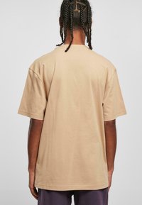 Beige Baumwoll-T-Shirt mit lockerer Passform, kurzen Ärmeln und rundem Halsauschnitt. Glatte Textur und minimale Details auf der Rückseite.