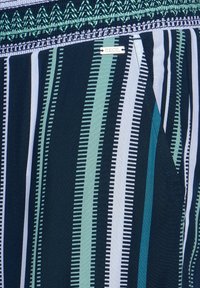 Granatowy materiał z pionowymi paskami w kolorze zielonym i białym, z teksturowanym pasem w talii i małą srebrną metką z napisem "CECIL."