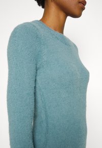 Ljusblå ulltröja med en mjuk, fluffig struktur, rund halsringning och figurnära passform. Sömdetaljer längs sidorna.