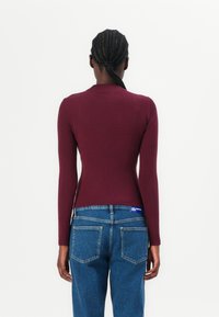 Bordeaux ribbel trui met lange mouwen en een aansluitende pasvorm, gecombineerd met high-waisted blauwe denim jeans met achterzakken.