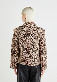 Leopardmønster jakke i brunt og svart, med en kraftig skulderdesign, med en strukturert passform og glatt tekstur. Kombinert med svarte bukser.