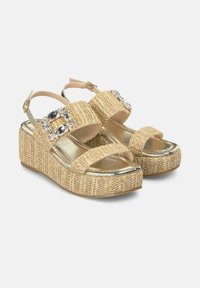 Sandali con zeppa e tomaia in simile paglia intrecciata, suola in oro metallizzato e gemme decorative trasparenti sulle cinghie. Fibbia regolabile alla caviglia.