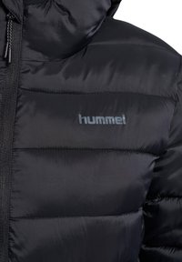 Czarna kurtka puchowa o pionowym pikowanym wzorze, wykonana z błyszczącej, gładkiej tkaniny. Posiada srebrne logo "hummel" na piersi oraz suwak.