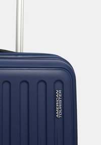 Valigia rigida della marina con scanalature verticali, superficie testurizzata e logo argento. Dispone di un manico retrattile e chiusura a zip.