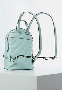 Sac à dos vert menthe matelassé avec bordure noire, bretelles doubles, poche avant zippée et texture lisse, présenté en angle.