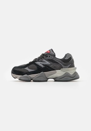 Baskets New Balance noires et grises avec empeigne en mesh et daim, semelle épaisse et rembourrée, et détail du logo rouge sur la languette.