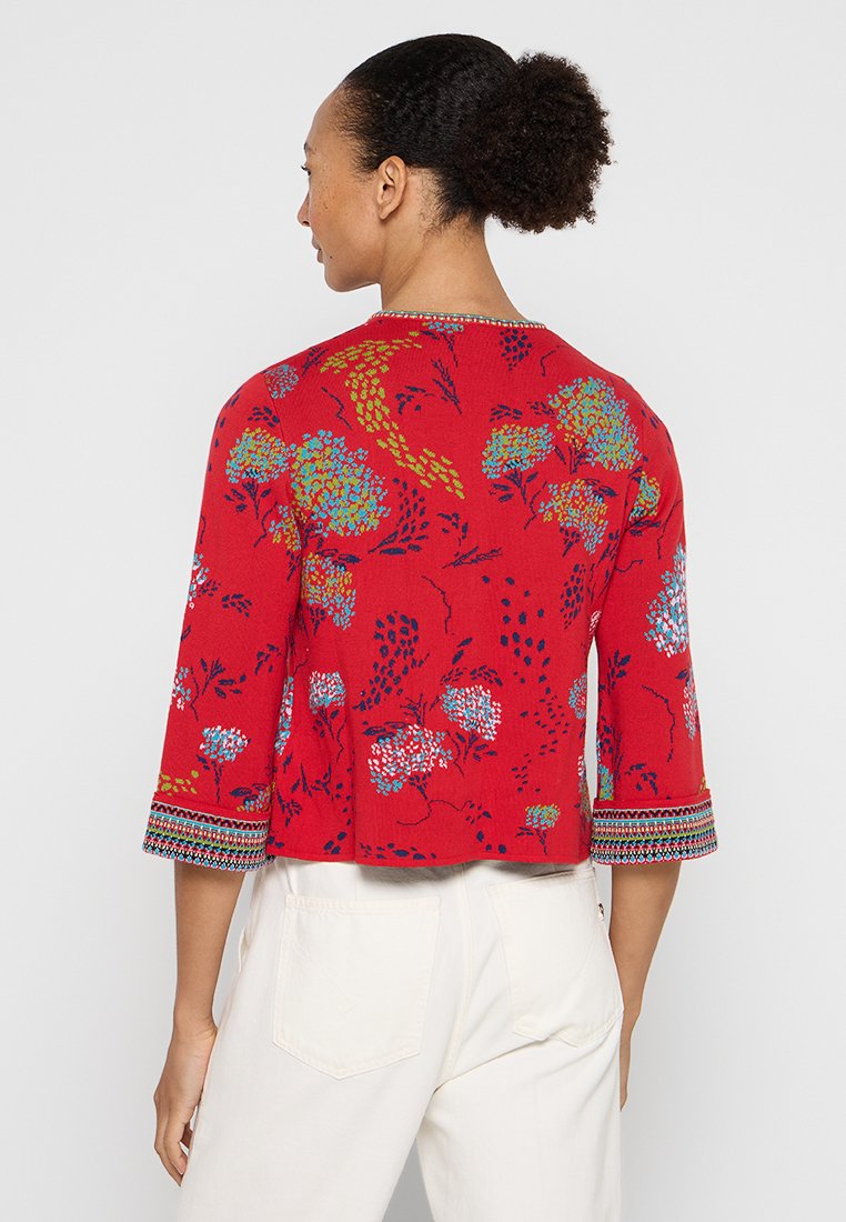 Czerwony, krótki top z rękawami z kwiatowym wzorem w odcieniach niebieskiego i zielonego. Posiada ozdobne wykończenie rękawów oraz luźny krój.