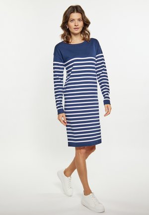 Tengerészkék, hosszú ujjú ruha fehér vízszintes csíkokkal, l boat neckline-nal és egyenes sziluettel, fehér sportcipőkkel párosítva.