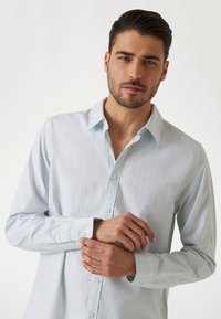 Camicia a maniche lunghe a righe blu chiaro e bianche con un design aderente. Presenta un colletto classico e polsini con bottoni.