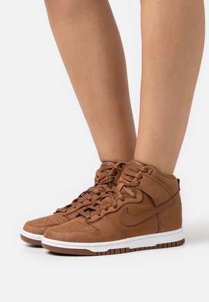 Braune Leder-Hochtop-Sneaker mit perforierter Zehenpartie, gepolstertem Kragen, weißer Sohle und seitlichem Logo. Die Schnürsenkel sind ordentlich gebunden.