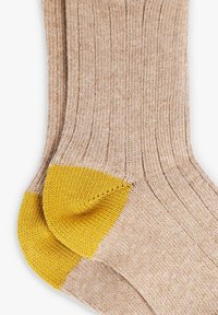 Calcetines de punto acanalado beige con talones reforzados de color amarillo brillante, dispuestos planos sobre un fondo blanco.