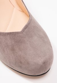 Gros plan d'une chaussure plate en daim taupe avec un bout légèrement pointu et des coutures lisses le long du bord supérieur.