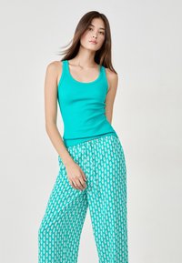 Débardeur à côtes turquoise associé à un pantalon ample avec un motif d'ananas blanc sur fond vert. Tissu doux, coupe décontractée.