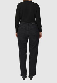 Jean noir fuselé taille haute, avec deux poches arrière et une texture en denim lisse, associé à un haut noir côtelé à manches longues.