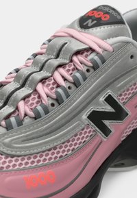 Roze i siva New Balance 1000 tenisica s mrežastim materijalom, reflektirajućim detaljima, crnim potplatom i rozim vezicama.