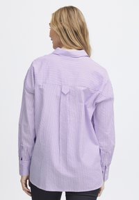 Purple and white striped button-up shirt, featuring a back yoke, single back pleat, and rounded hem, made from lightweight fabric.