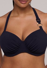 Donkerblauwe bikini-top met een geplooid ontwerp, voorzien van verstelbare bandjes en een gouden ronde accent op één bandje. Glad, textuurstof.