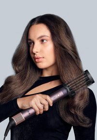 Fohnborstel met een cilindrische zwarte borstelkop en een roze handvat met knoppen en ventilatiesleuven; model met halflang, golvend haar.