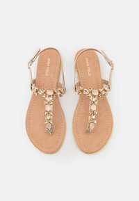 Beiga faux läder flip-flops med en dekorativ rem som har klara och rosa stenar. Gula detaljer på sulan. Justerbar vristrem.