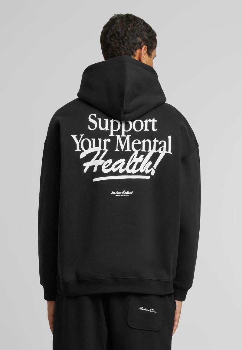 Sudadera negra con un gran texto gráfico blanco en la parte trasera que dice "¡Apoya tu salud mental!" y un logotipo más pequeño cerca del dobladillo.