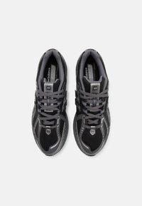 Chaussures de sport noires et grises avec une tige en mesh, un col rembourré, un embout renforcé, et des lacets. Elles comportent des accents réfléchissants et une semelle texturée.