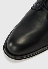 Pantof din piele neagră, cu suprafață netedă, vârf rotunjit și cusături de-a lungul marginii tălpii.