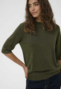 Maglione verde oliva a maniche corte realizzato in morbido tessuto a maglia, con taglio dritto e orlo a costine, caratterizzato da una silhouette rilassata.