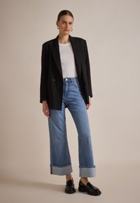 Sacou negru, supradimensionat peste un tricou alb ajustat, asociat cu blugi largi, cu talie înaltă, de un albastru deschis, cu margini răsucite și mocasini negri.