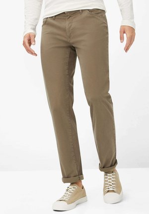 Chino en coton marron avec une coupe slim, présentant un devant plat et des poignets roulés, associés à des baskets beige à lacets.