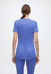 Εφαρμοστό μωβ αθλητικό τοπ με κοντά μανίκια και καμπυλωτό τελείωμα, κατασκευασμένο από λείο, ελαστικό υλικό. Λεπτομέρεια ραφής τρέχει κάθετα στην πλάτη.