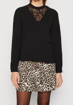 Zwarte lange mouwen top met kant driehoek detail bij de halslijn, gedragen met een dierenprint rok. Soepele textuur, aansluitend ontwerp en zichtbare naden.
