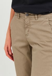 Pantaloni in cotone beige con vestibilità slim, dotati di tasche anteriori, frontale piatto e chiusura a un singolo bottone. Tessuto liscio, design leggero.