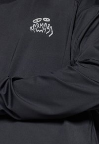 Black long-sleeve shirt with a smooth texture featuring white "KARMA" graphic design on the left chest area. Simple, modern design.