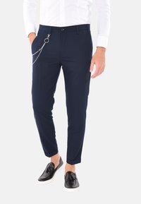 Pantaloni navy in tessuto lavorato, con un accento a catena sulla tasca laterale, taglio slim e risvolti. Abbinati a scarpe nere slip-on.