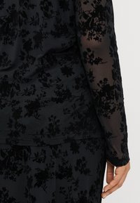 Robe noire à motif floral avec de longues manches semi-transparentes. Le matériau semble doux, présentant une texture veloutée détaillée et de délicates broderies.