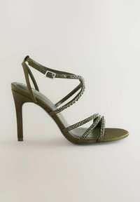 Sandalo con tacco a stiletto verde oliva, dal design con cinturini, decorato con strass trasparenti, dotato di cinturino alla caviglia e una finitura liscia e lucida.