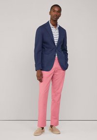 Granatowa marynarka na paski, w zestawieniu z jasnoróżowymi spodniami i beżowymi loafersami. Gładkie faktury, dopasowany krój, klasyczny design.