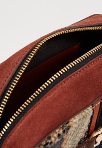 Interno di una borsa in suede marrone con zip dorata; fodera nera e dettaglio in pelle di serpente testurizzata all'esterno.