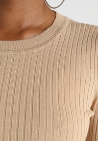 Beige geripptes Stricktop mit Rundhalsausschnitt und figurbetontem Schnitt. Die Textur ist glatt und hat definierte vertikale Linien.