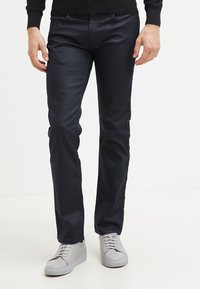 Marinblå byxor i slim fit, tillverkade av en mjuk textil, med en klassisk design som inkluderar framfickor och i kombination med ljusgrå sneakers.