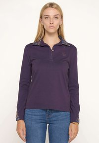 Polo à manches longues de couleur violette avec un col et des poignets à motifs, doté d'une patte de boutonnage et d'un logo brodé sur la poitrine.