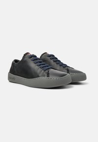 Black leather sneakers with navy blue laces, featuring a grey rubber sole and contrasting stitching along the edges. Minimalist design.
