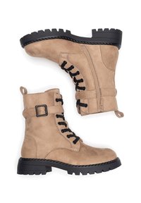 Botines beige de ante con cordones negros, cremallera lateral y detalle de hebilla. Suela gruesa de goma negra con dibujo pronunciado.