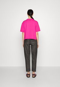 Rosa verkürztes T-Shirt aus Baumwolle, kurze Ärmel, kombiniert mit dunkelgrauen Slim-Fit-Hosen und schwarzen Sandalen mit rosa Akzenten.