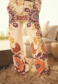 Pantaloni a gamba larga in tessuto crema con vivaci motivi floreali in arancione, viola, verde e blu. Design con vita elastica.