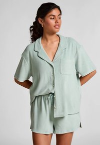 Korte mouwen pyjama set in licht mintgroen, gemaakt van zachte stof. Het overhemd heeft een zak en knoopsluiting; de korte broek heeft een elastische tailleband.