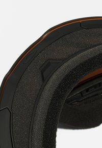 Sort hjelminterior med mat overflade, skumpolstring og en orange accent. Har en vinkelret design med synligt hardware til justering af pasform.